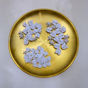 Organized sets of white crown flower beads in a gold tray, perfect for DIY jewelry, car leis, and wedding decorations.