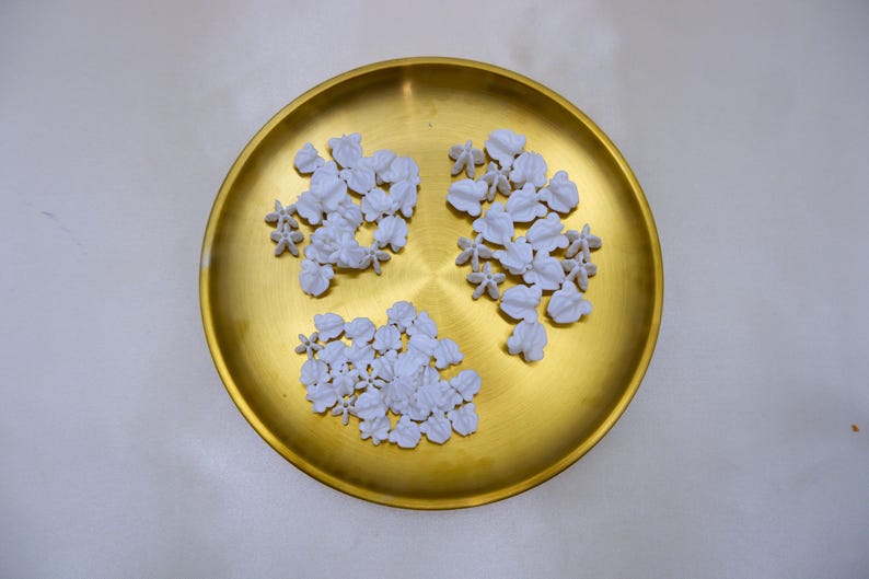 Organized sets of white crown flower beads in a gold tray, perfect for DIY jewelry, car leis, and wedding decorations.