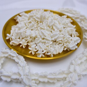 Durable white plastic crown flower beads for lei making arranged with a completed flower garland in a decorative gold tray.
