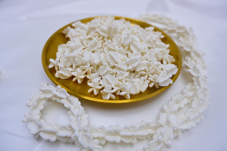 Durable white plastic crown flower beads for lei making arranged with a completed flower garland in a decorative gold tray.