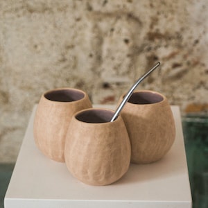 Può includere: Tre tazze in ceramica marrone con una cannuccia in metallo argentato. Le tazze hanno una superficie testurizzata e sono disposte a forma di triangolo.