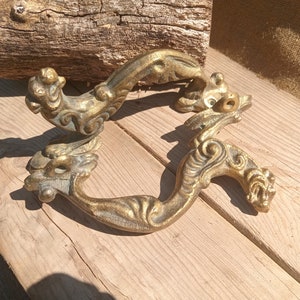 Può includere: Un paio di maniglie per porte in metallo dorato ornate con un motivo a drago. Le maniglie sono riccamente dettagliate e hanno un aspetto vintage.