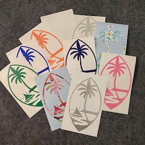 May include: A collection of oval-shaped stickers featuring palm tree designs in various colors, including blue, orange, green, and pink. Some stickers have additional elements like boats and floral patterns. The stickers are on a gray surface.