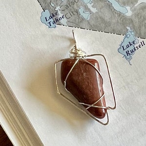 May include: A brown gemstone pendant wrapped in silver wire, creating a geometric shape. The pendant is displayed on a map with the text "Lake Tahoe City" visible.