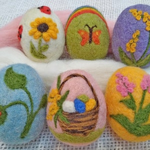 May include: Six felt Easter eggs decorated with spring-themed embroidery. The eggs are in various colours, including white, light blue, light pink, yellow, green, and purple. The designs include a sunflower, a butterfly, a basket of flowers, a ladybug, and a sprig of leaves.