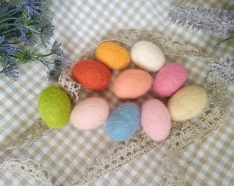 May include: Nine felt Easter eggs in various pastel colors, including green, yellow, orange, pink, blue, and white. The eggs are arranged in a circle on a checkered tablecloth.