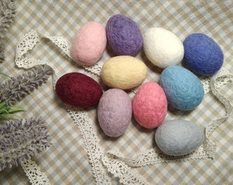 May include: Nine felt Easter eggs in various colors, including pink, purple, white, blue, beige, gray, and maroon. The eggs are arranged in a circle on a checkered fabric background.