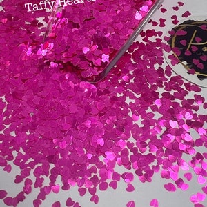 May include: A scoop filled with pink glitter hearts, with more hearts scattered around the scoop. The text "Taffy Hearts" is visible on the scoop.