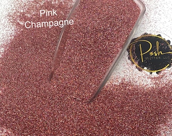 Puede incluir: Purpurina fina de color champán rosa en una pala de plástico transparente sobre un fondo blanco. La purpurina es fina, brillante y ligeramente iridiscente. El texto "Pink Champagne" es visible en la imagen.