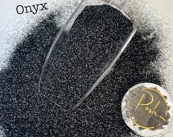 May include: A scoop of black glitter with the word "Onyx" written above it. The glitter is spread out on a white surface and a small round sticker with the word "Posh" is in the lower right corner.