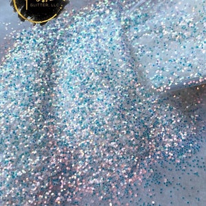 May include: Close-up of opalescent glitter with a .6mm particle size. The glitter is a mix of blue, pink, and white, creating a shimmering effect. The text "OPALINE .6MM" is visible in the image.