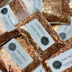 K&ouml;nnte beinhalten: Klare Plastikt&uuml;ten gef&uuml;llt mit einer Mischung aus goldenem, kupferfarbenem und rotem Glitzer. Jede T&uuml;te hat ein wei&szlig;es Etikett mit dem Text "Free Fallin'" und dem PoshGlitter-Logo. Der Glitzer ist eine Mischung aus Formen und Gr&ouml;&szlig;en.