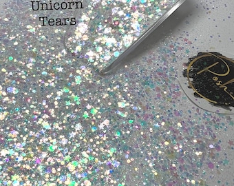 May include: A close-up of iridescent glitter in various shapes and sizes, including stars and circles. The glitter is white with a rainbow sheen. The text "Unicorn Tears" is visible in the image.