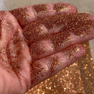 May include: A close-up of a hand covered in fine copper glitter. The glitter is very sparkly and has a metallic sheen.
