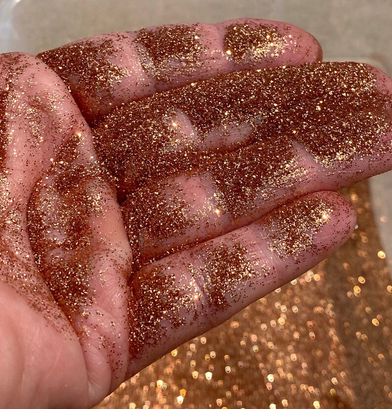May include: A close-up of a hand covered in fine copper glitter. The glitter is very sparkly and has a metallic sheen.