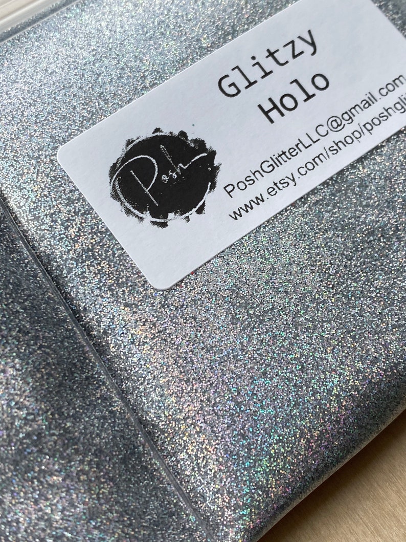 May include: A package of silver glitter labeled "Glitzy Holo." The glitter is contained in a clear plastic bag. The label includes the Etsy shop name and contact information.