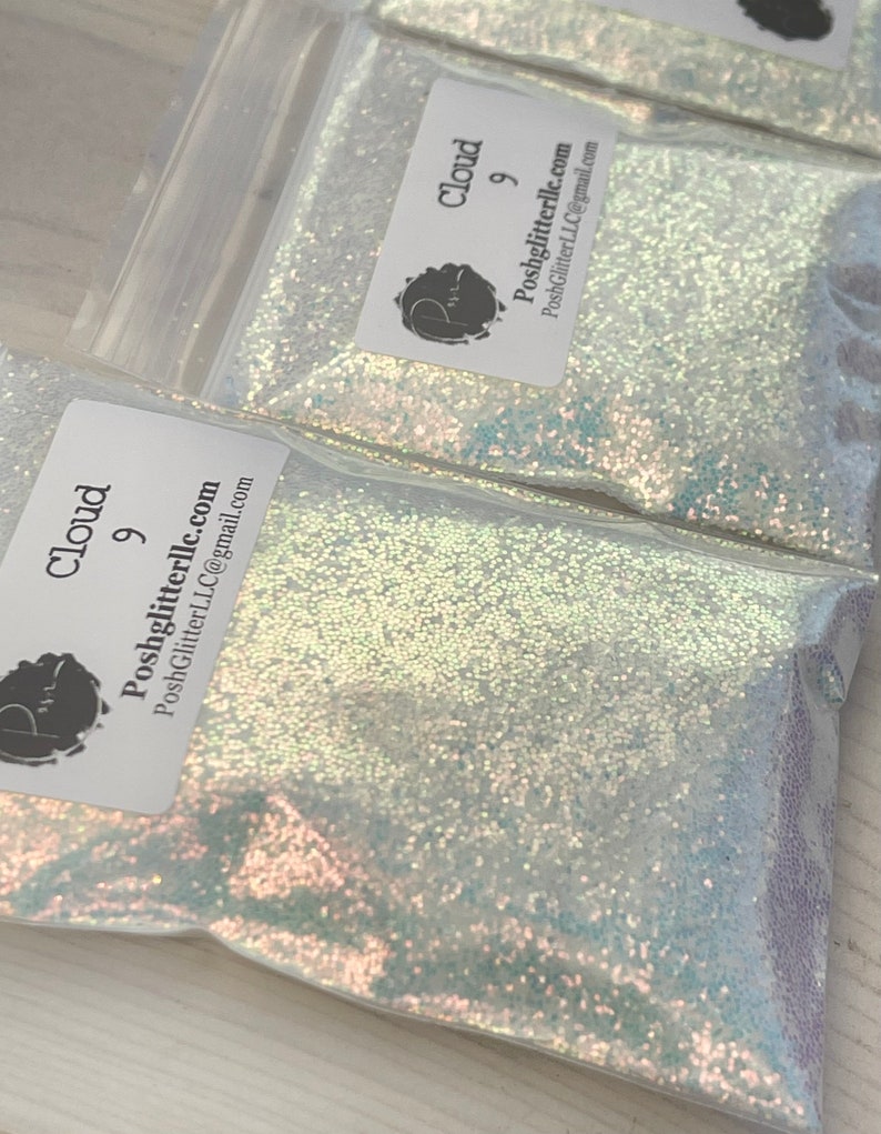 May include: A clear plastic bag filled with iridescent white glitter. The bag has a label that says "Cloud 9" and "Poshglitterllc.com".