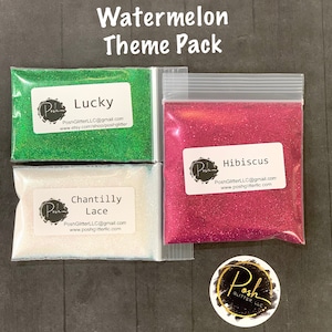 May include: Three small bags of glitter, labeled "Lucky", "Chantilly Lace", and "Hibiscus". The glitter is green, white, and pink, respectively. The bags are arranged in a row on a dark surface. The image also includes a small circle sticker with the text "Posh Glitter, LLC".