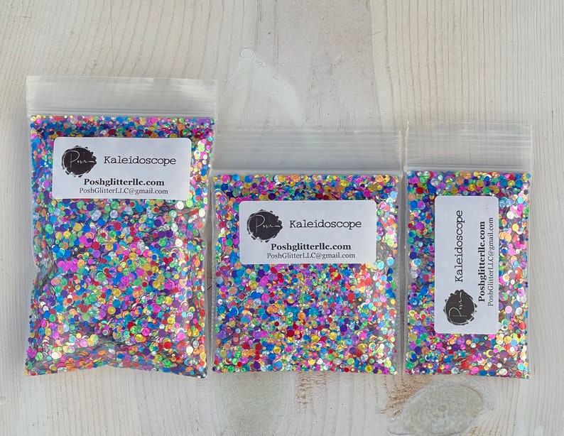 May include: Three clear plastic bags filled with colorful glitter. Each bag has a white label with the text "Kaleidoscope" and the seller's logo and contact information. The glitter appears to be a mix of various shapes and colors, including pink, blue, green, and yellow.