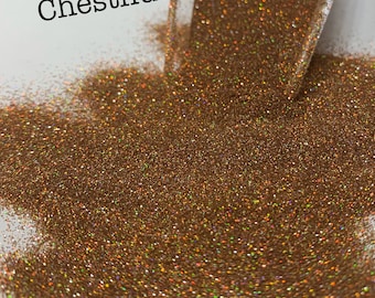May include: A close-up of a pile of iridescent brown glitter with a scoop in the background. The text "Chestnut Holo" is visible in the top left corner of the image.