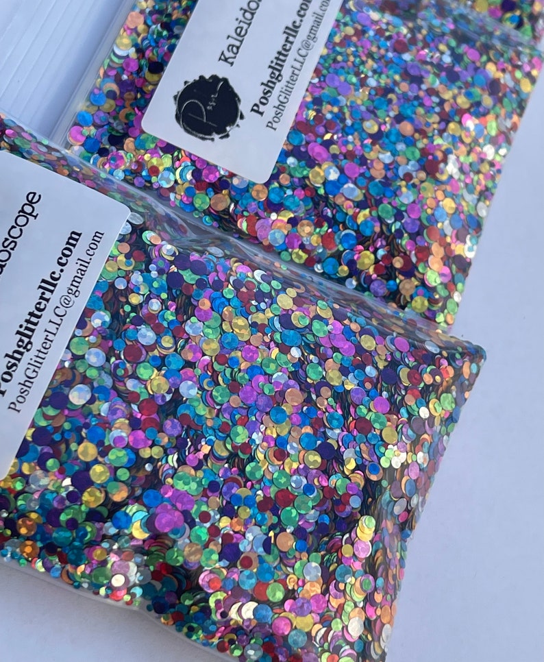 May include: Two clear plastic bags filled with colorful, iridescent glitter. The glitter is a mix of round shapes in various colors, including blue, purple, green, and gold. Each bag has a white label with the text "Kaleidoscope" and "PoshGlitterLLC.com".