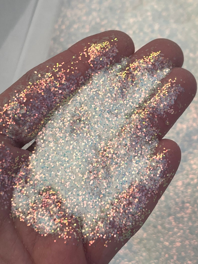 May include: A close-up of iridescent glitter in a hand. The glitter is a mix of white, silver, and gold.