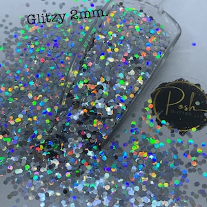 May include: A close-up of iridescent silver glitter, 2mm in size, in a clear plastic scoop. The glitter is scattered around the scoop, creating a shimmering effect. The text "Glitzy 2mm" is visible in the top left corner of the image.