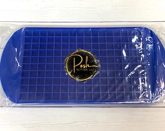 Puede incluir: Una bandeja de cubitos de hielo de silicona azul con 100 cuadrados individuales. La bandeja está empaquetada en plástico transparente y tiene el logotipo "Posh Glitter, LLC" impreso en ella.