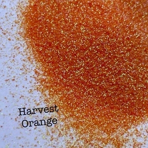 May include: A close-up of orange glitter with a fine, shimmery texture. The glitter is labeled "Harvest Orange".