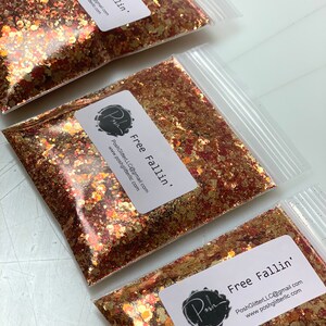 K&ouml;nnte beinhalten: Klare Plastikt&uuml;ten gef&uuml;llt mit goldenem, kupferfarbenem und rotem Glitzer. Jede T&uuml;te hat ein wei&szlig;es Etikett mit dem Text "Free Fallin'" und dem Posh-Logo. Der Glitzer hat verschiedene Formen und Gr&ouml;&szlig;en.