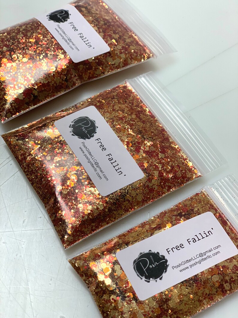 K&ouml;nnte beinhalten: Klare Plastikt&uuml;ten gef&uuml;llt mit goldenem, kupferfarbenem und rotem Glitzer. Jede T&uuml;te hat ein wei&szlig;es Etikett mit dem Text "Free Fallin'" und dem Posh-Logo. Der Glitzer hat verschiedene Formen und Gr&ouml;&szlig;en.