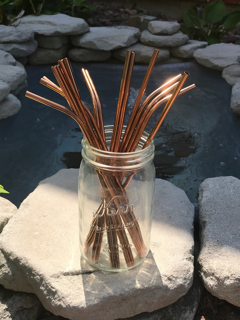 May include: A glass jar filled with a bundle of reusable copper drinking straws. The jar is labeled "Kerr Self Sealing Mason Jar".