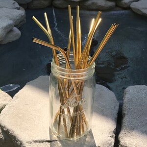 May include: A glass jar filled with a bundle of gold metal drinking straws. The jar is sitting on a gray rock.