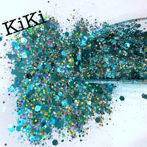 May include: Teal, iridescent glitter with a variety of sizes and shapes. The glitter is scattered on a white surface and the word "Kiki" is written in black at the top of the image.