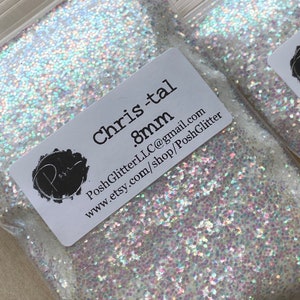 Puede incluir: Dos bolsas de pl&aacute;stico transparente llenas de purpurina iridiscente. Cada bolsa tiene una etiqueta blanca con el texto "Chris-tal .8mm" y el nombre y la direcci&oacute;n del sitio web de Etsy. La purpurina parece ser una mezcla de blanco y colores pastel.