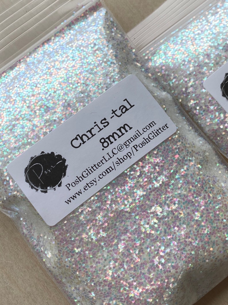 Puede incluir: Dos bolsas de pl&aacute;stico transparente llenas de purpurina iridiscente. Cada bolsa tiene una etiqueta blanca con el texto "Chris-tal .8mm" y el nombre y la direcci&oacute;n del sitio web de Etsy. La purpurina parece ser una mezcla de blanco y colores pastel.