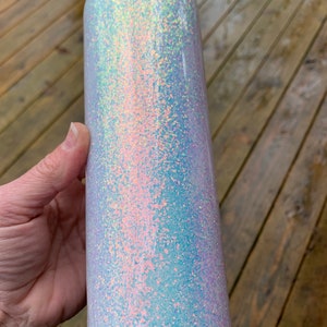 May include: A white tumbler with iridescent glitter. The glitter is a mix of light blue, pink, and white.