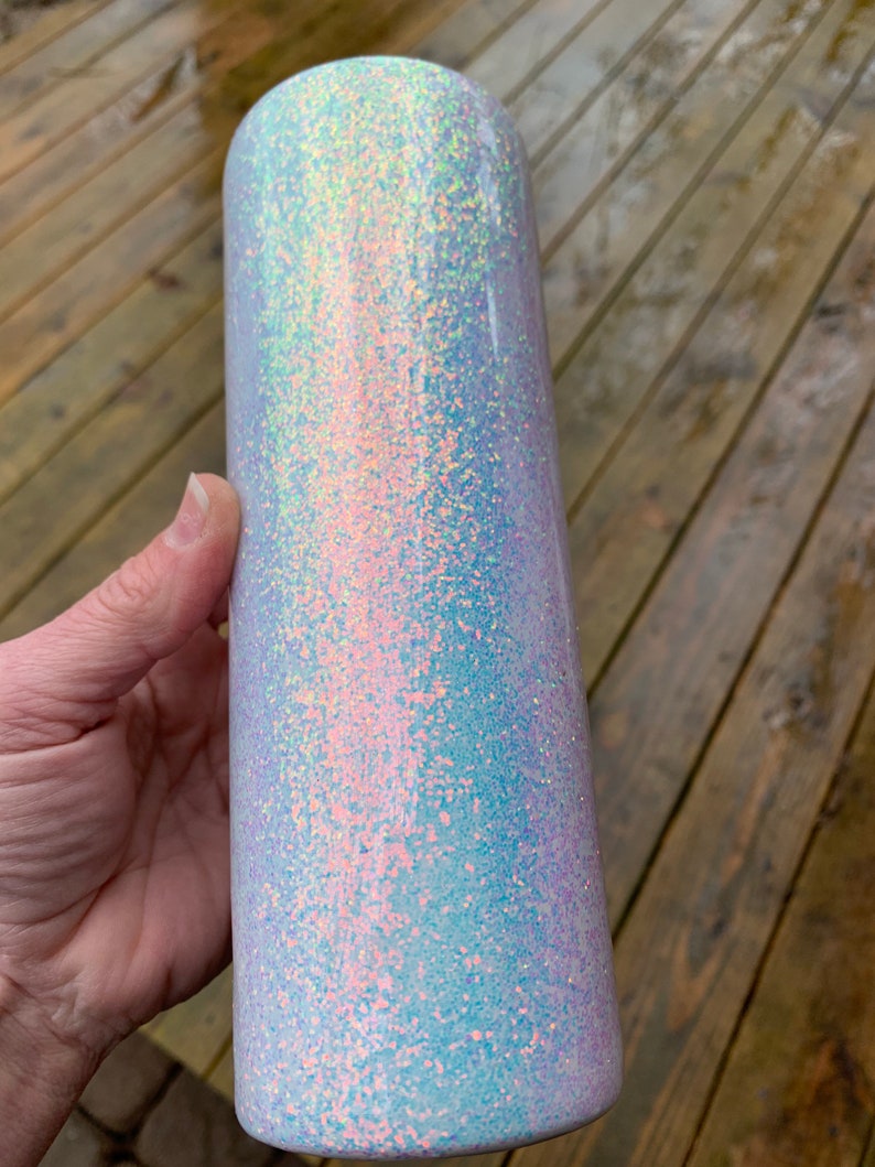 May include: A white tumbler with iridescent glitter. The glitter is a mix of light blue, pink, and white.