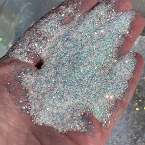 May include: A close-up of iridescent white glitter with a subtle blue shimmer. The glitter is spread out on a hand, showcasing its texture and sparkle.