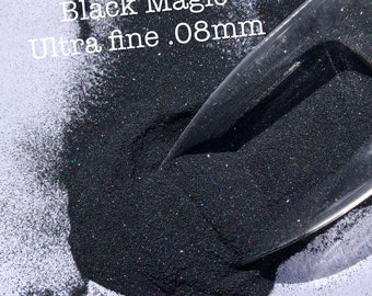 May include: Black glitter, labeled "Black Magic Ultra fine .08mm", shown in a pile on a white surface. A clear plastic scoop is partially buried in the glitter.