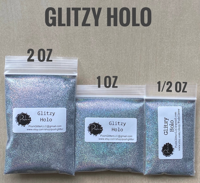 May include: Three clear plastic bags filled with silver glitter. The bags are labeled with the text "GLITZY HOLO" and sizes 2 OZ, 1 OZ, and 1/2 OZ. Each bag has a white label with the brand name and contact information.