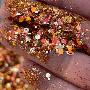 K&ouml;nnte beinhalten: Nahaufnahme einer Handvoll Glitzer in Gold-, Kupfer- und Rosat&ouml;nen. Die Glitzerpartikel sind eine Mischung aus kleinen Punkten und gr&ouml;&szlig;eren sechseckigen Formen, die einen funkelnden Effekt erzeugen. Ideal f&uuml;r Bastelarbeiten und Dekorationen.