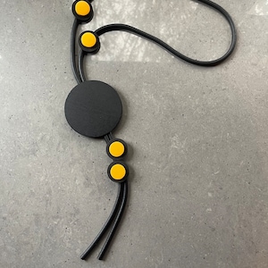 Black rubber necklace, with large black and small yellow wooden round shapes.