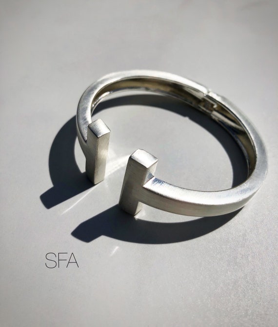Stunning geo, brushed matt silver. With T design. On a spring fastener.