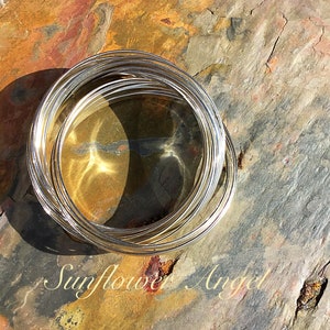 May include: A stack of silver wire rings on a textured brown and orange rock surface. The text "Sunflower Angel" is visible below the rings.