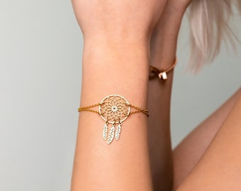 May include: A gold chain bracelet with a dreamcatcher charm. The charm is detailed with a circular design and dangling feathers.