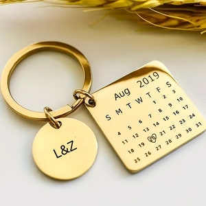May include: Gold-toned keychain with a small round charm engraved with "L&Z" and a larger square charm with a calendar for August 2019. The date "29" is circled with a heart.