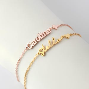May include: Two delicate name bracelets. One is rose gold with the name "Caroline" and a cross charm. The other is gold with the name "Stella" and a heart charm. Both bracelets have a chain link design.
