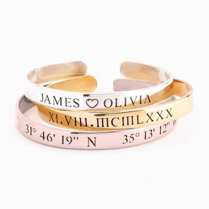 May include: Three stacked bracelets with engraved text. The top bracelet is silver and says "JAMES ♥ OLIVIA". The middle bracelet is gold and says "XI.VII.MCIII LXX". The bottom bracelet is rose gold and says "31° 46' 19" N 35° 13' 12" ".