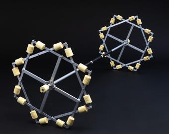 May include: Two silver fire fans with a black handle. Each fan has a geometric design with multiple beige wicks attached. The fans are connected by a silver rod and are set against a black background.